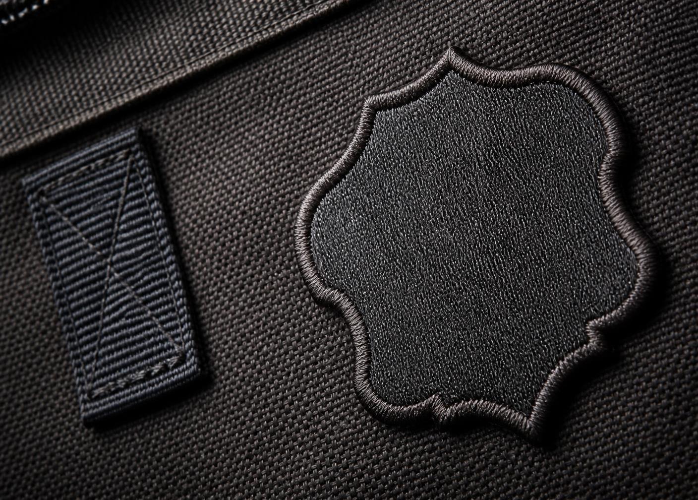 Close-up of an embroidered badge and woven label stitched onto charcoal bag fabric